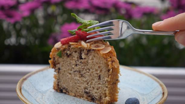 A slice of cake topped with fresh strawberries, mint leaves, and almond slices, with a fork ready to take a bite.