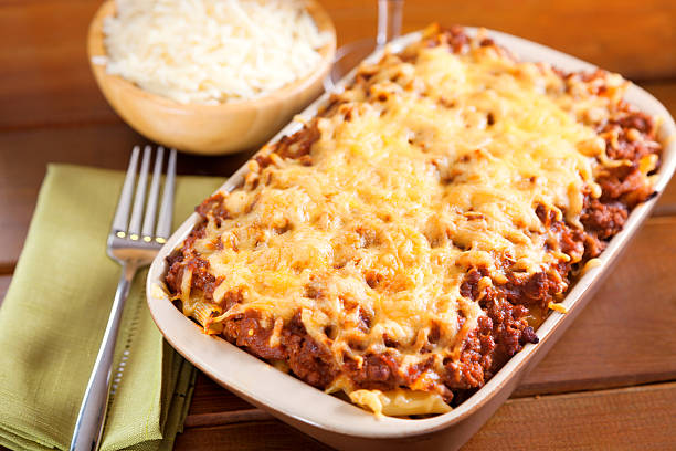 A casserole dish filled with cheesy baked pasta topped with ground meat and sauce, served with a side of shredded cheese in a bowl.