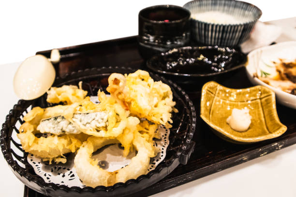 A plate of tempura sushi and sides, including wasabi and dipping sauces on a black tray.