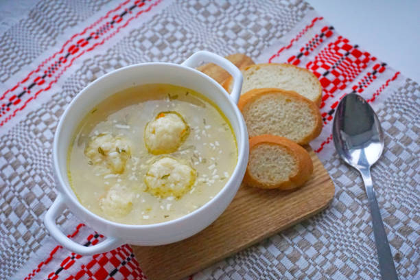 Freshly made soup with dumplings served in a white bowl next to slices of bread on a wooden cutting board.