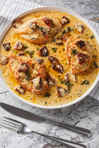 Creamy baked chicken breasts garnished with sun-dried tomatoes and herbs in a white serving dish