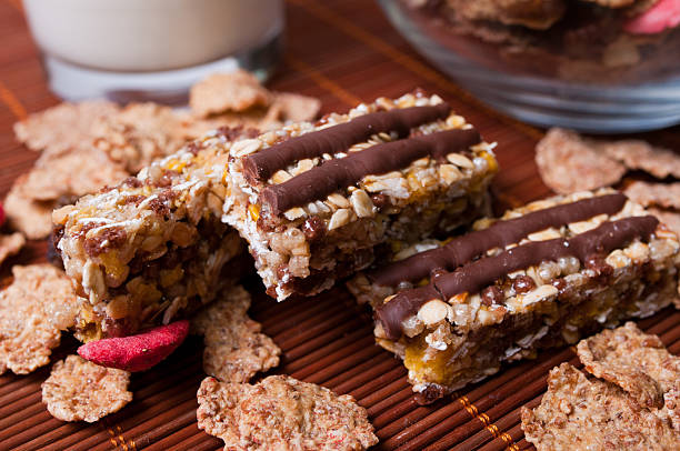 Delicious homemade granola bars drizzled with chocolate, placed on a bamboo mat alongside cereal flakes.