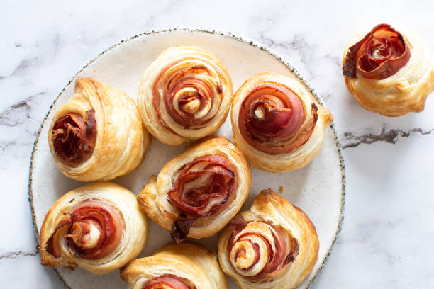 A plate of freshly baked ham and cheese spiraled pastries on a marble surface.
