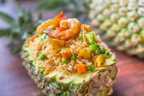 A vibrant serving of fried rice topped with shrimp and colorful vegetables, presented in a hollowed-out pineapple.