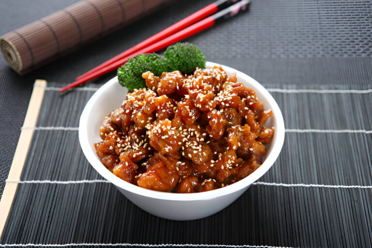 A bowl of sesame chicken garnished with sesame seeds and broccoli.