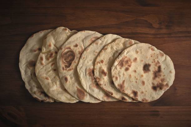 A stack of freshly baked flatbreads on a wooden surface.
