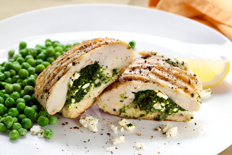 Stuffed chicken breast with spinach and feta cheese on a plate with green peas and a lemon wedge.