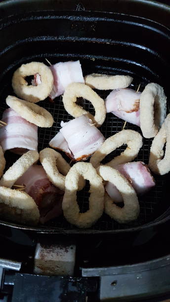 An air fryer basket containing pieces of bacon-wrapped food and round breaded items.