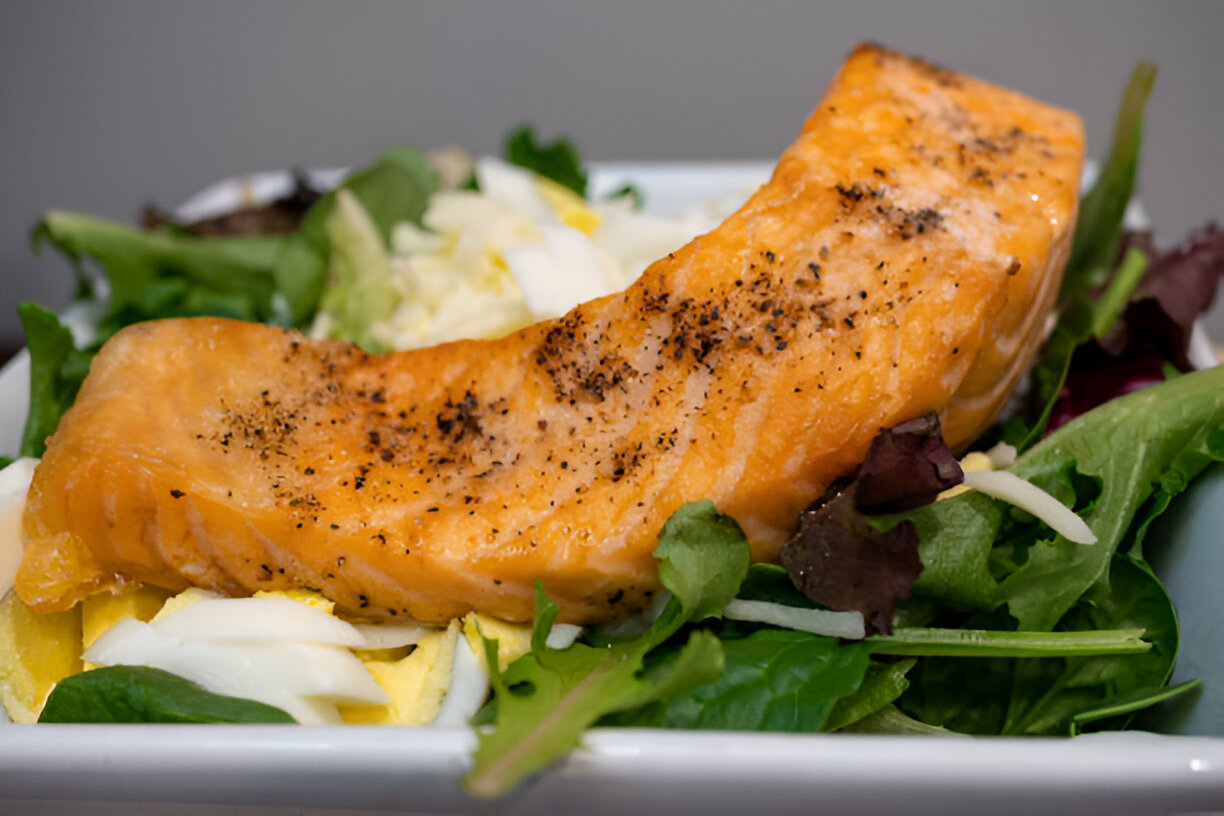 A vibrant dish featuring a piece of salmon resting on a bed of mixed greens and vegetables.