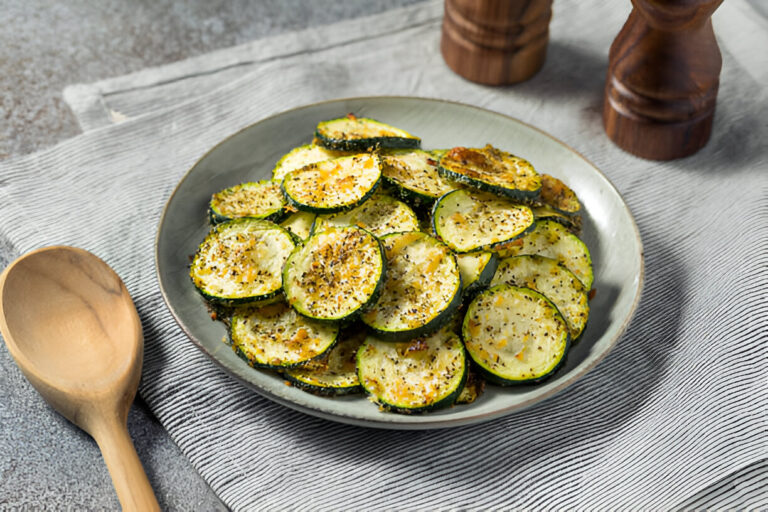A plate of crispy baked zucchini chips seasoned with herbs and spices, placed on a striped kitchen towel.