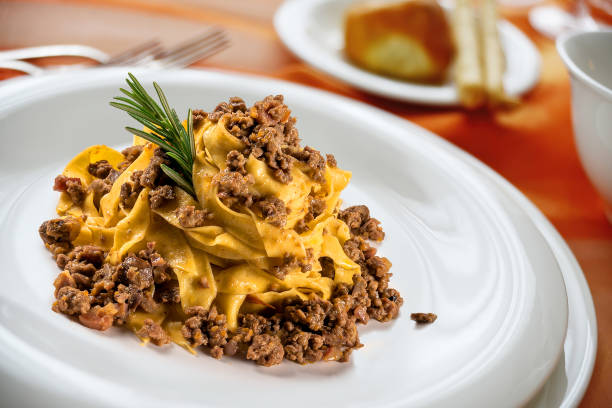 Plate of fettuccine pasta topped with minced beef and a sprig of rosemary.