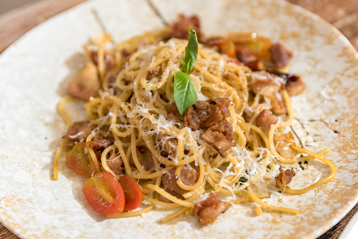 A plate of spaghetti topped with shrimp, bacon, cherry tomatoes, and a sprinkle of cheese garnished with fresh basil.