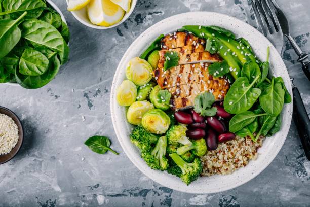 A healthy bowl featuring grilled chicken, quinoa, broccoli, Brussels sprouts, green beans, and fresh spinach, garnished with sesame seeds and cilantro.