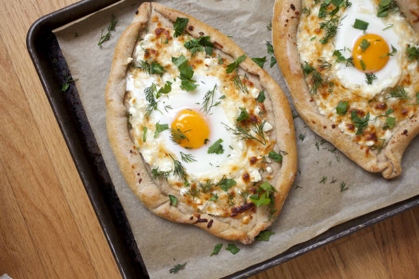 Two freshly baked khachapuri with eggs and herbs on a baking tray