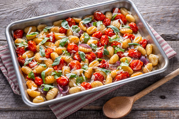 A tray of gnocchi with roasted cherry tomatoes and fresh basil on a wooden surface.