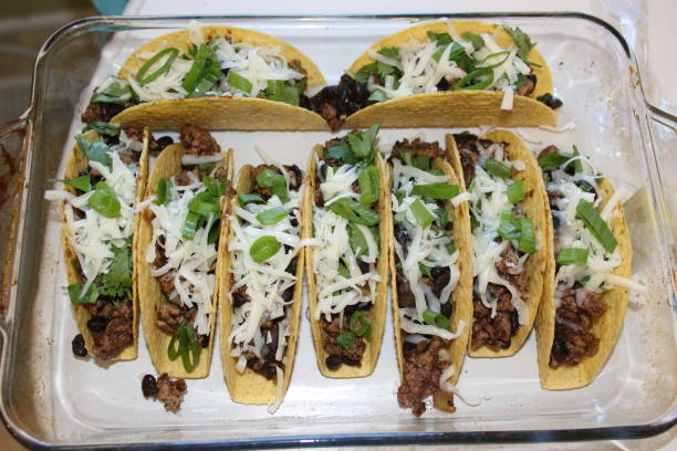 A platter of tacos filled with ground beef, black beans, shredded cheese, and green onions.