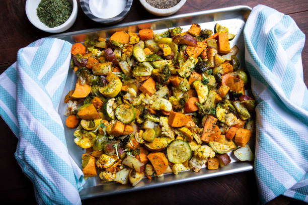 A tray of roasted vegetables including sweet potatoes, zucchini, and carrots, garnished with herbs, on a wooden table.