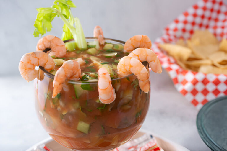 A glass of seafood cocktail garnished with shrimp and celery, served alongside tortilla chips