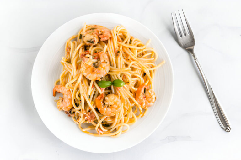 A bowl of shrimp pasta with vibrant colors and a basil leaf garnish, served with a fork on the side.