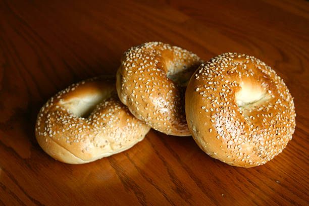 Three sesame seed bagels stacked on a wooden table