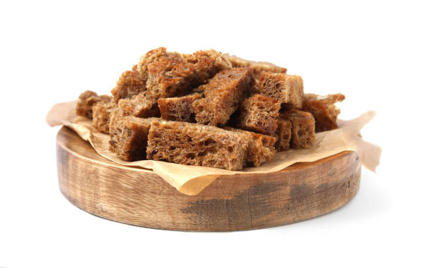 A wooden plate with a pile of brown bread croutons on parchment paper.