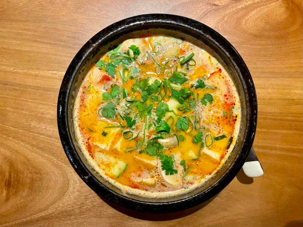 A bowl of vibrant soup topped with fresh herbs and green onions, served on a wooden table.