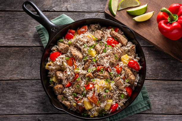 A skillet filled with beef and rice topped with colorful vegetables like red peppers and green onions.