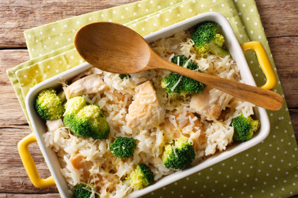 A casserole dish filled with rice, chicken pieces, and broccoli, with a wooden spoon resting on top.