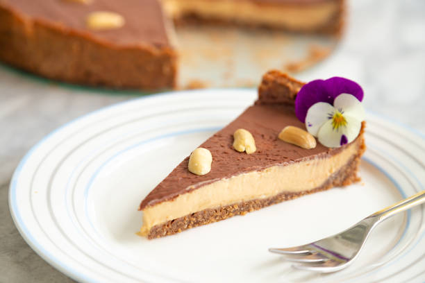 A slice of chocolate and peanut butter cheesecake on a plate, garnished with a violet flower and peanuts.
