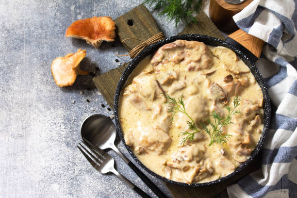 Creamy dish with pieces of meat and herbs served in a black bowl on a wooden cutting board.