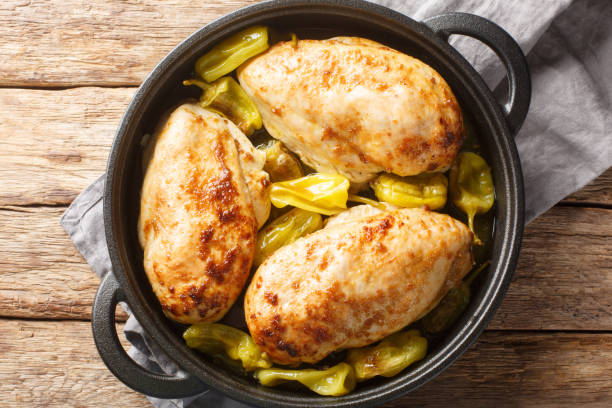 Cooked chicken breasts with yellow peppers in a black pot on a wooden surface.