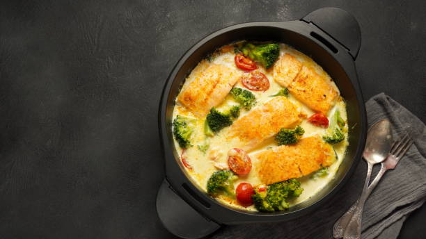 Baked salmon fillets with broccoli and cherry tomatoes in a black casserole dish