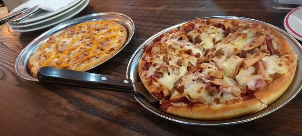 Two pizzas on metal trays, one loaded with toppings and cheese, and one with a simple cheese topping.