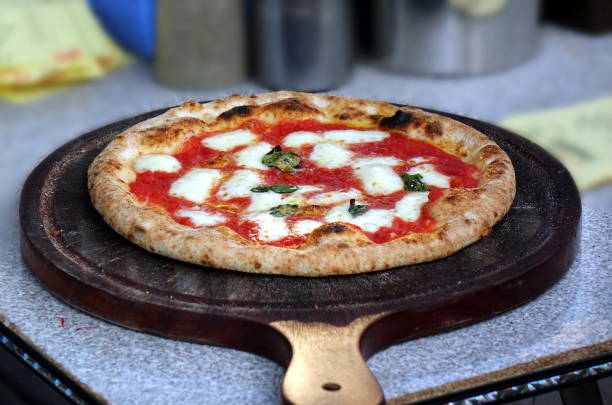 Freshly baked Margherita pizza with mozzarella and basil on a wooden pizza peel.
