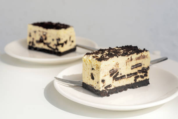 Two slices of Oreo cheesecake on white plates with forks.