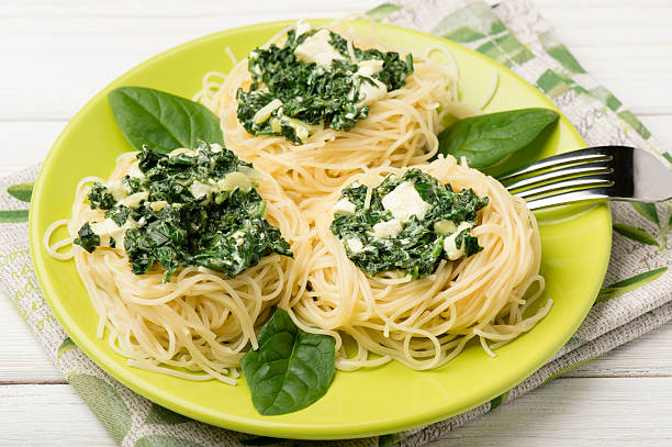 Three servings of spaghetti topped with creamy spinach and cheese on a vibrant green plate, surrounded by fresh spinach leaves.