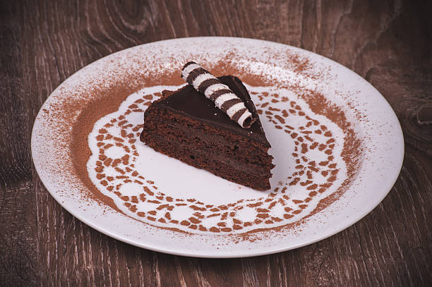 A slice of rich chocolate cake on a decorative plate sprinkled with cocoa powder.