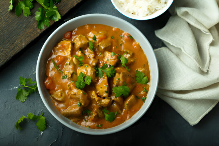 A bowl of delicious chicken curry garnished with fresh cilantro, surrounded by rice and a cloth napkin.