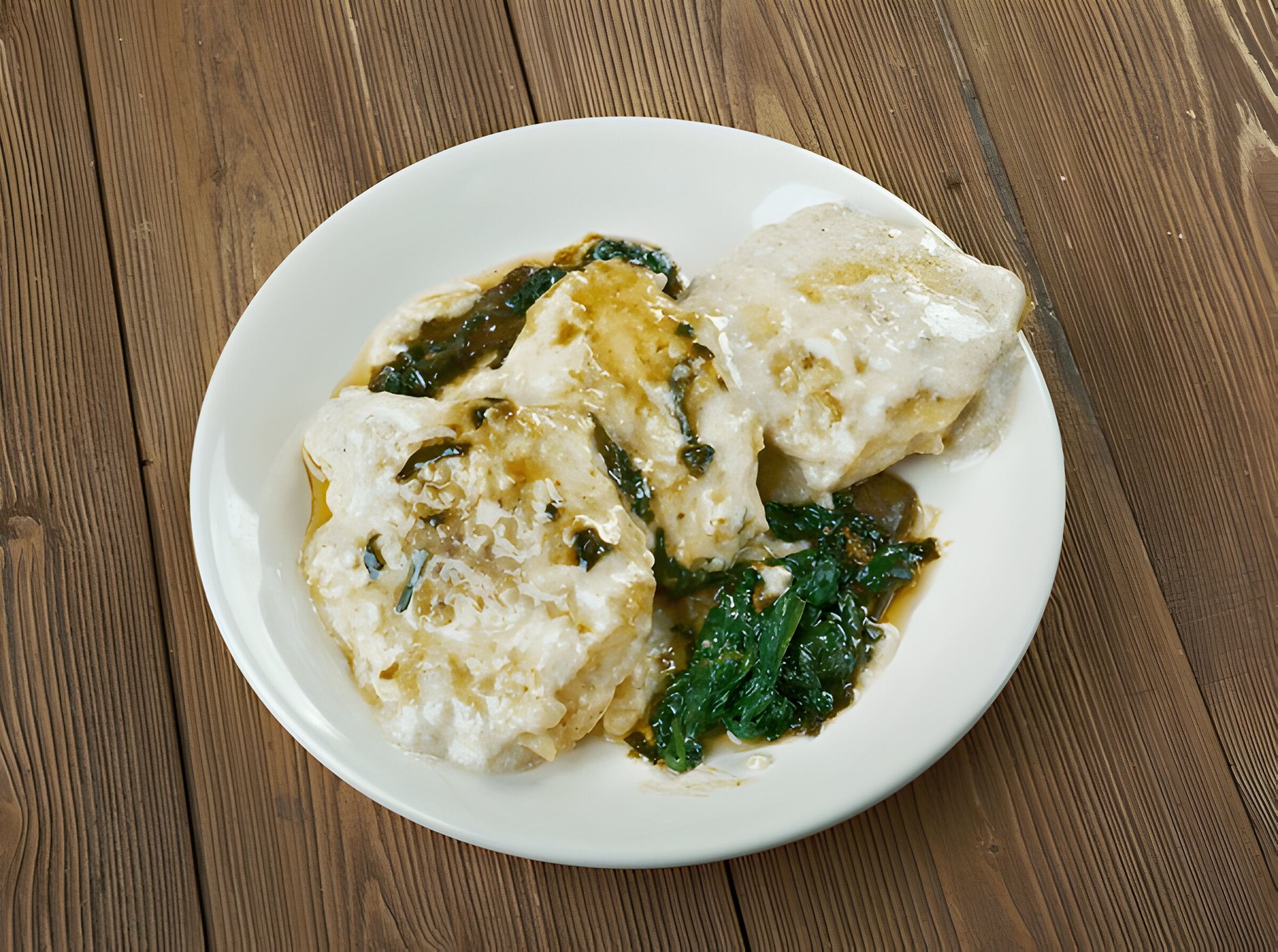 A plate of savory dumplings served with leafy greens and a dark sauce on a wooden table.