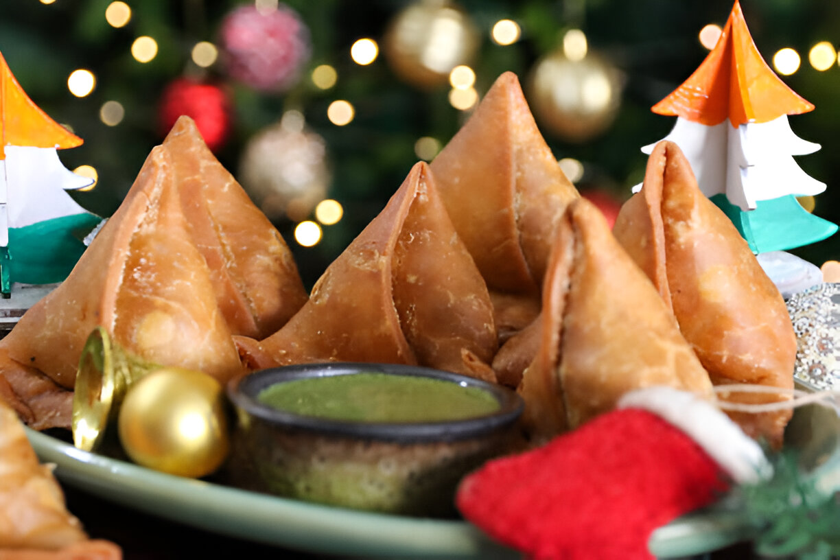 A plate of golden-brown samosas served with green chutney, adorned with festive decor.