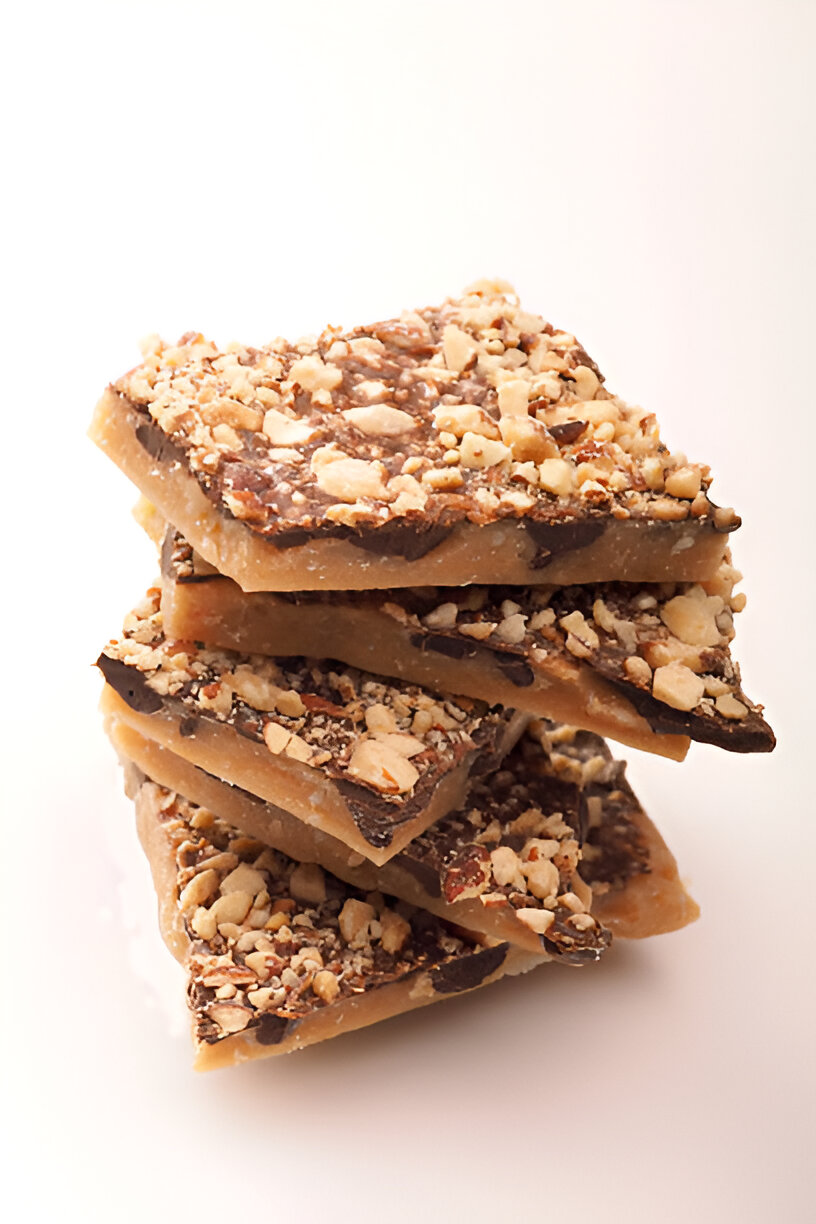 A stack of crunchy toffee pieces topped with chocolate and chopped nuts.