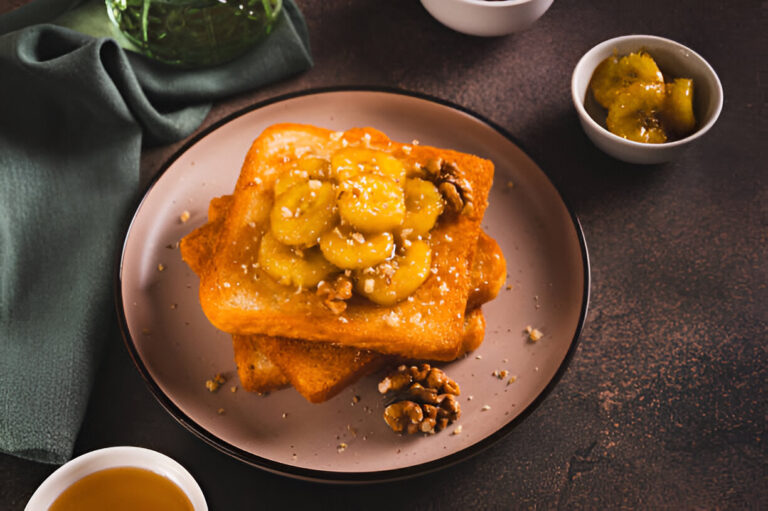 A delicious serving of French toast topped with sliced bananas and walnuts on a round plate.