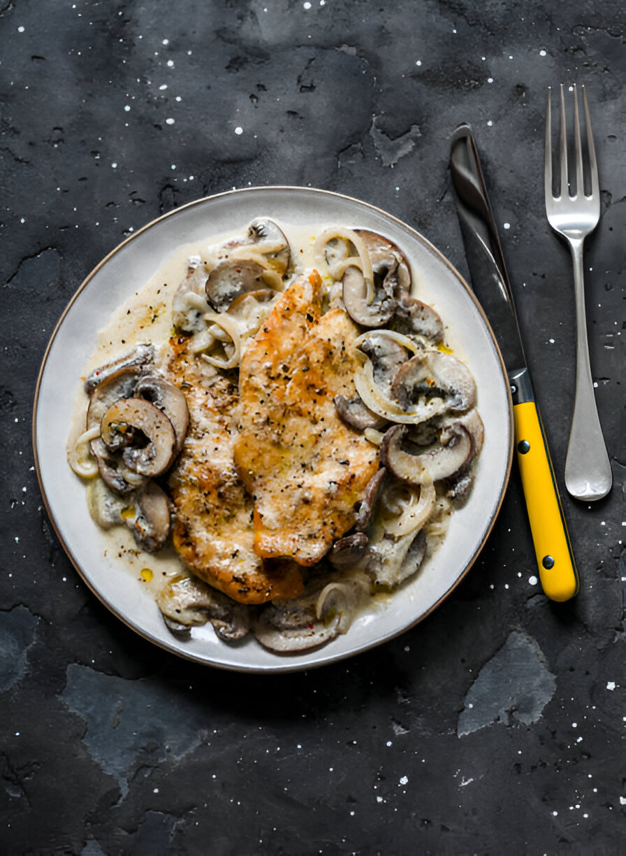 A plate of creamy chicken with mushrooms and onions served on a dark textured background.
