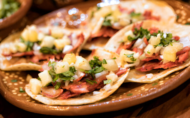 Close-up of tacos topped with pineapple, onion, and cilantro on a decorative plate.
