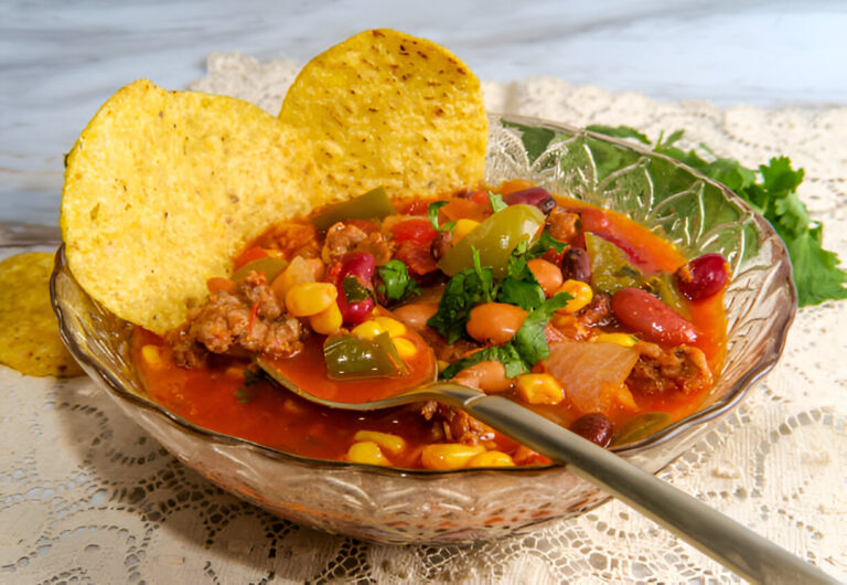 A bowl of hearty beef chili topped with fresh cilantro and served with tortilla chips.