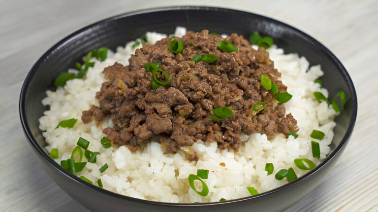 A bowl of white rice topped with a serving of seasoned ground beef and sprinkled with chopped green onions.