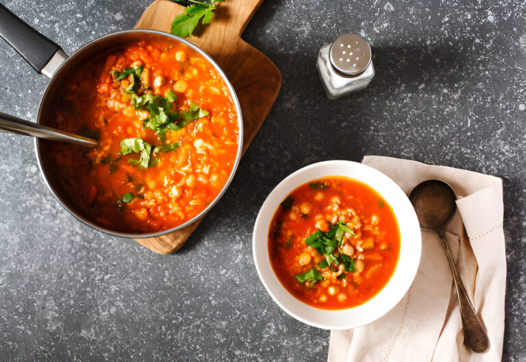A pot of soup on a wooden cutting board next to a bowl of soup garnished with fresh herbs
