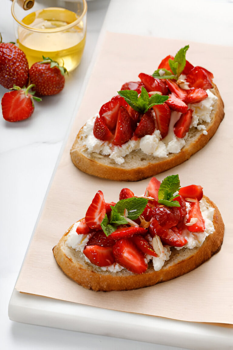 Two slices of bread topped with fresh strawberries and mint leaves on a white surface.