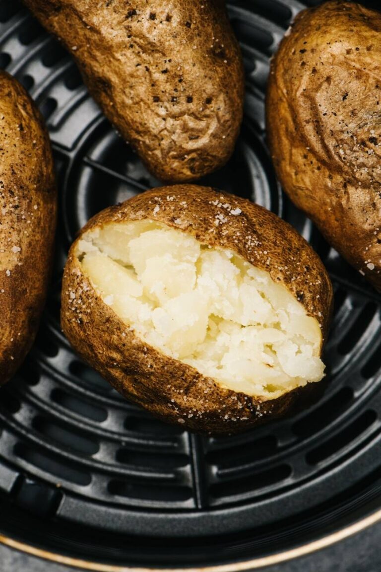 Baked potatoes with a crispy brown skin, one cut open to reveal fluffy white insides, sprinkled with salt.