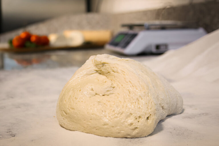 A smooth ball of pizza dough resting on a marble countertop with flour sprinkled around it.